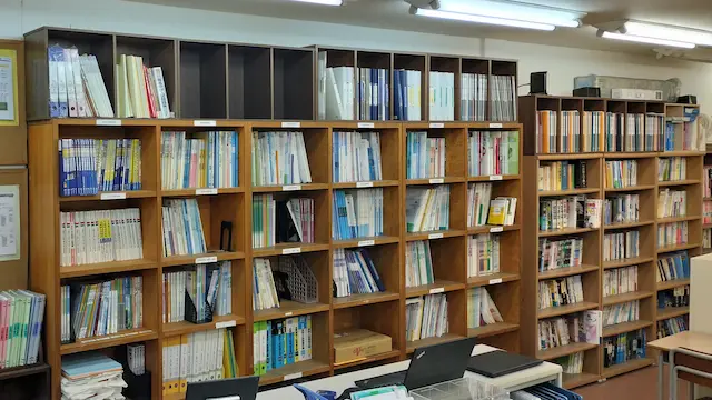 英語・数学・国語・理科・社会の教材が並ぶ教室の教材棚